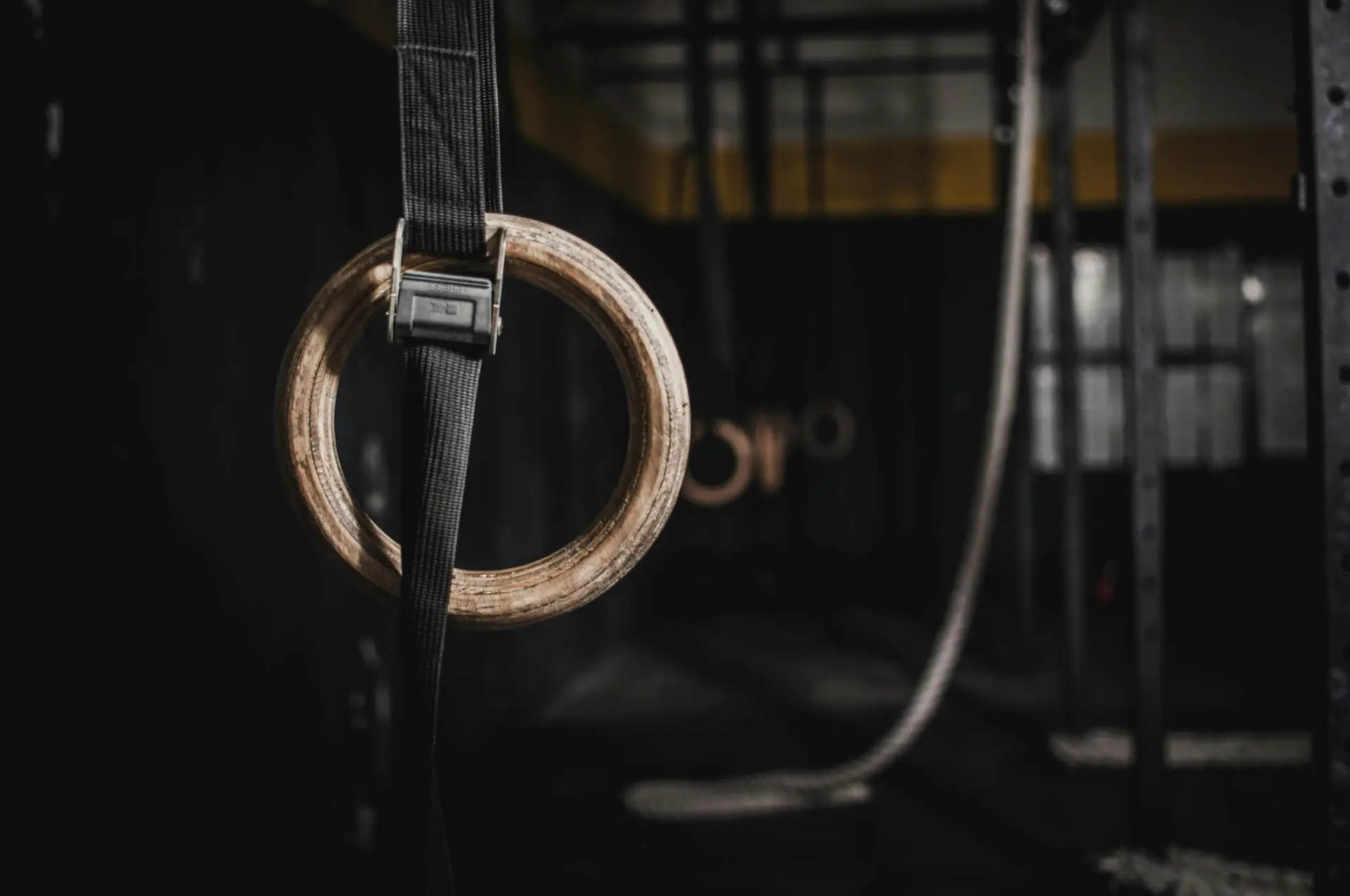 Close-up of a wooden gymnastic ring hanging in a dimly lit indoor gym, emphasizing fitness and training.