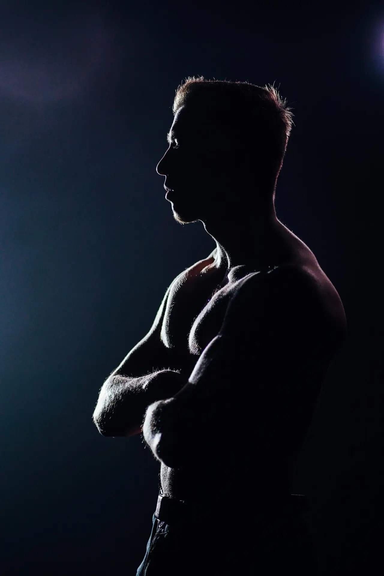 Silhouette of a muscular man striking a pose, backlit, with a dramatic and artistic feel.
